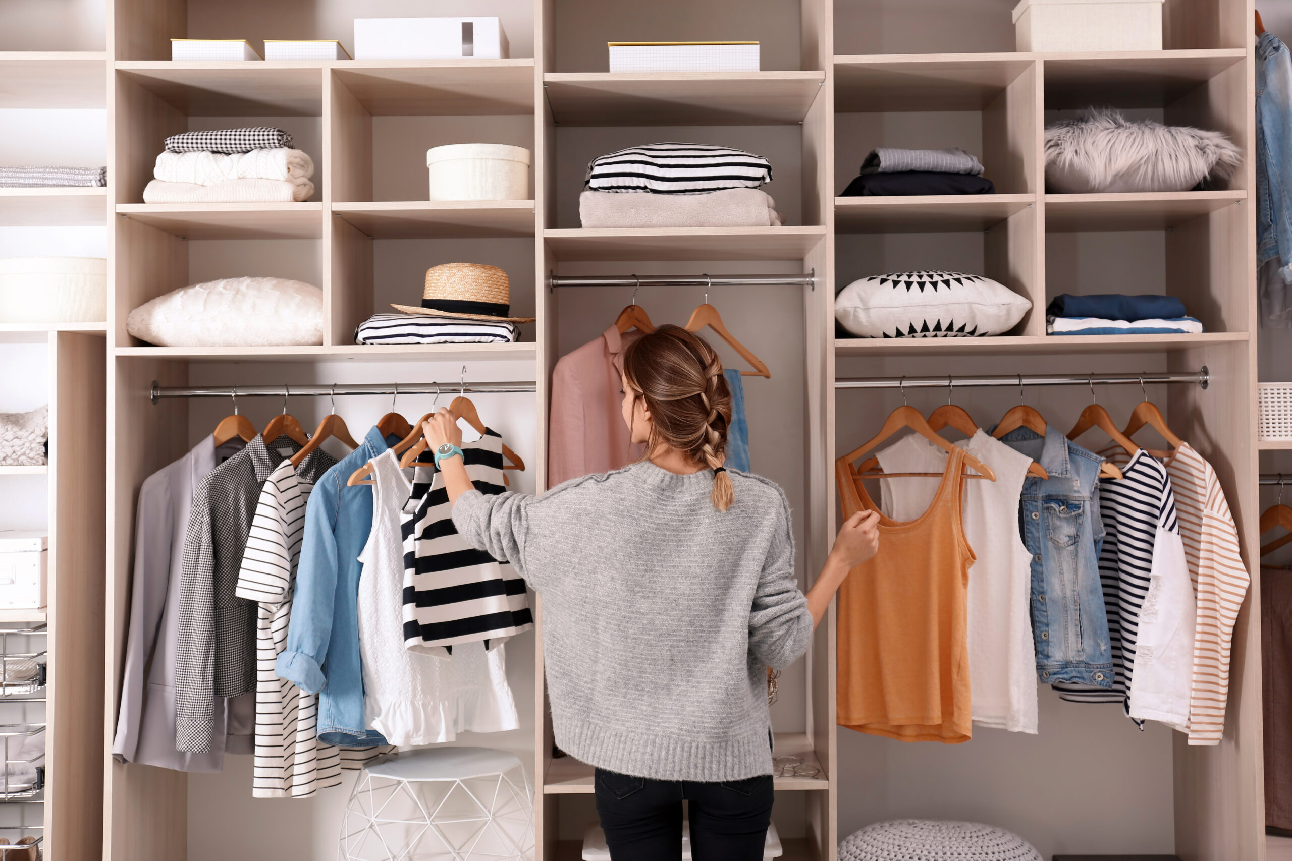 A woman stands in front of an organized closet, selecting a striped top among neatly arranged clothes and accessories. The scene conveys a tidy, stylish vibe.