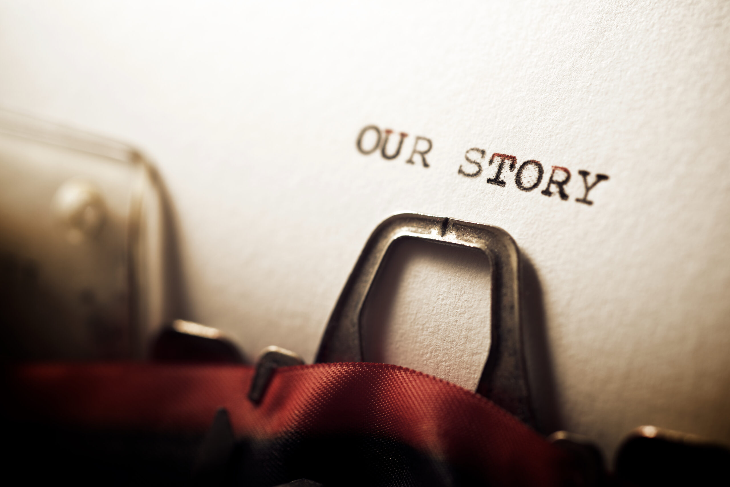 Close-up of a typewriter typing "OUR STORY" on white paper. The focus is on the text, conveying nostalgia and the beginning of a narrative.